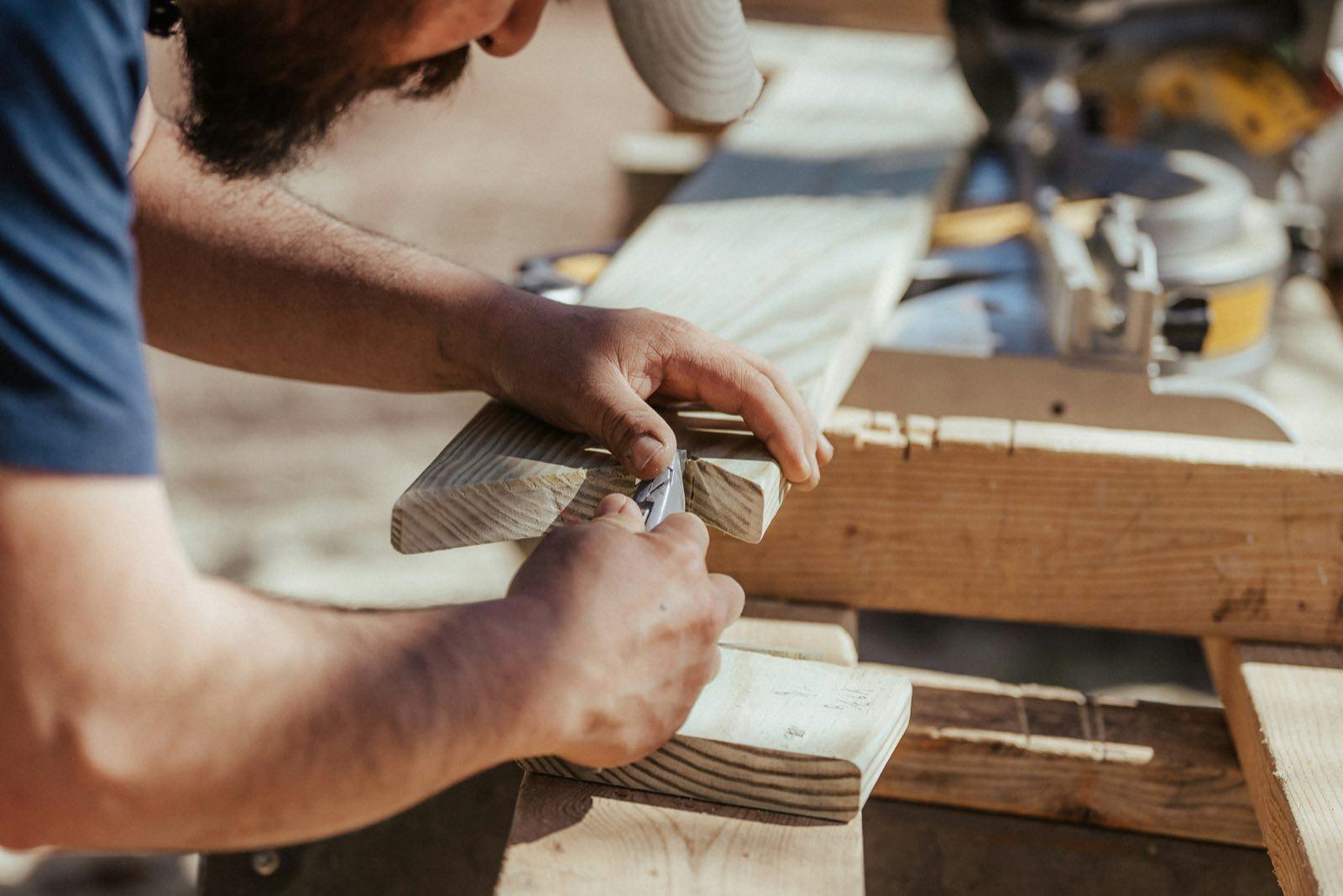 Close-up of carpenter's hands trimming a lumber offcut with a utility knife near a miter saw