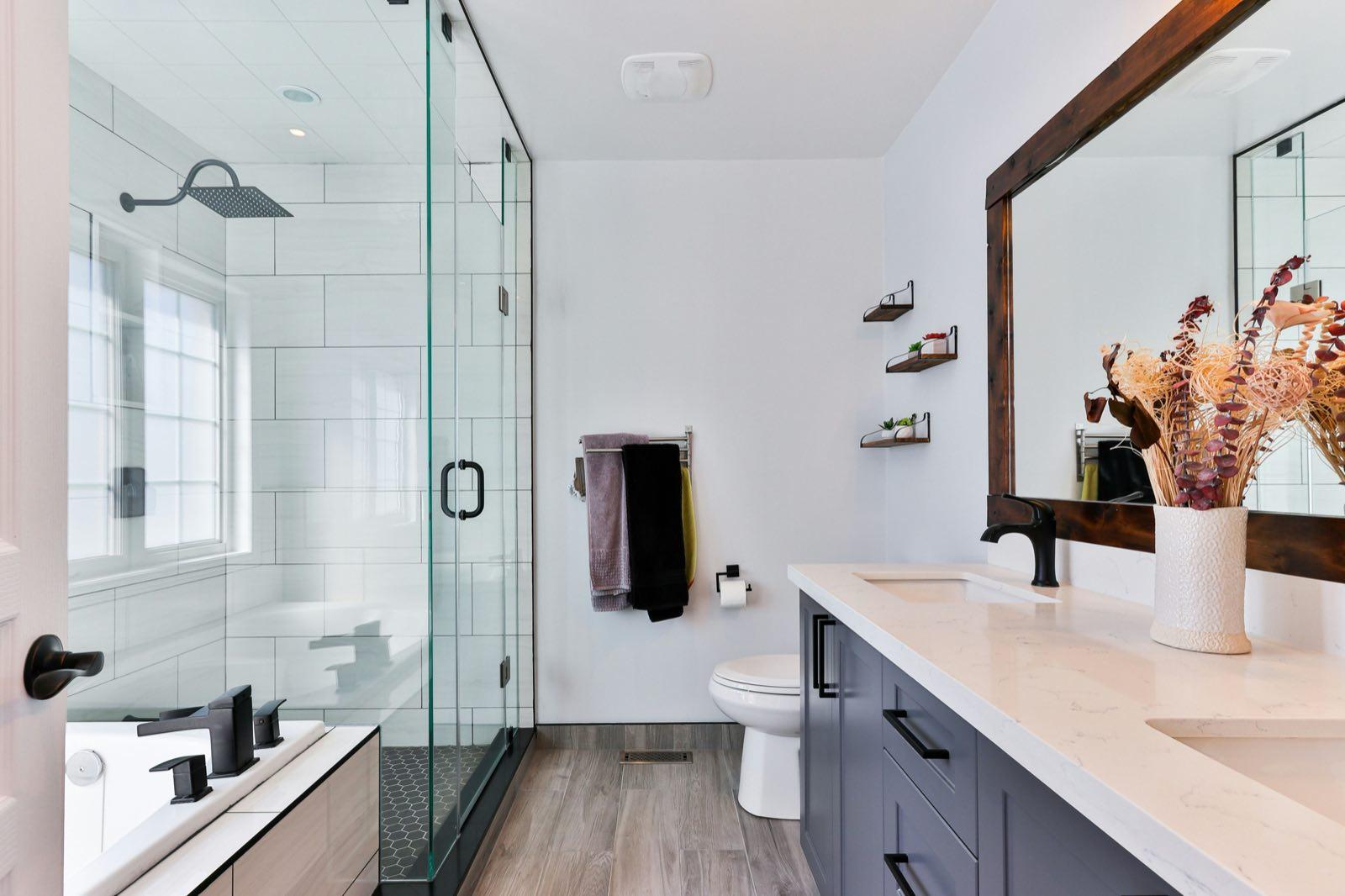 Remodeled bathroom with a glass shower enclosure, double quartz vanity, and wood-framed mirror