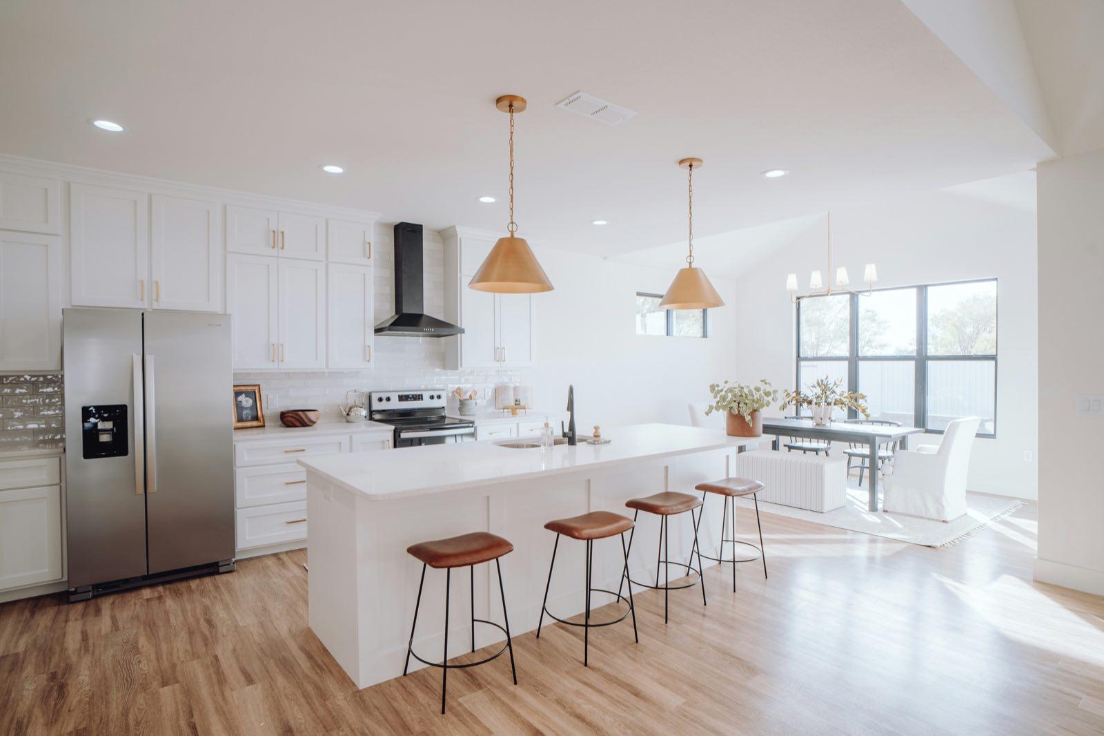 Open-plan white kitchen with a quartz island, bar seating, and adjoining dining area