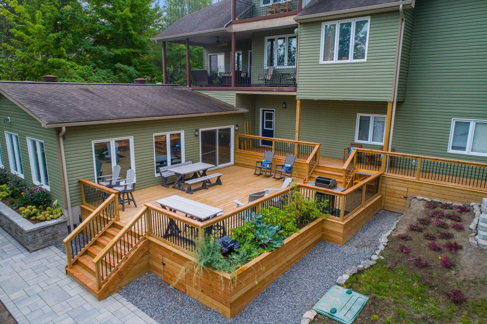 Multi-level cedar deck with built-in planter beds, bench seating, and stairs to a paver patio