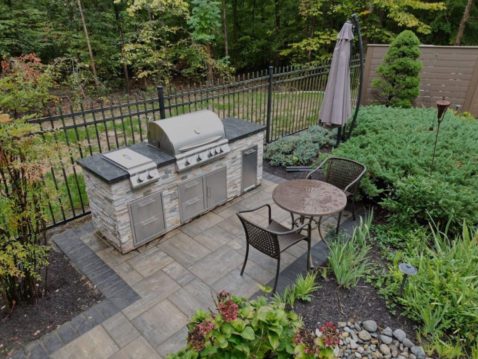 Built-in stone outdoor kitchen with a stainless grill beside a deck