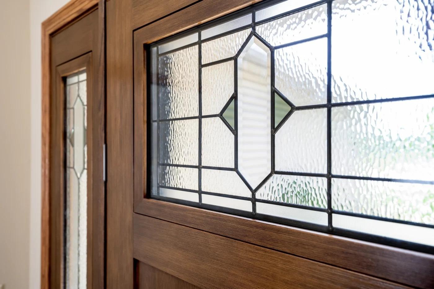 Close-up of leaded decorative glass panel in a wood-grain entry door with matching sidelight