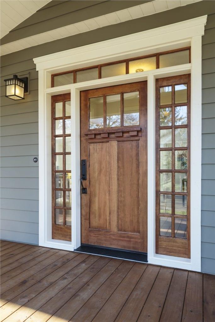 Craftsman stained-wood front door with divided-light sidelights and transom on a gray-sided porch