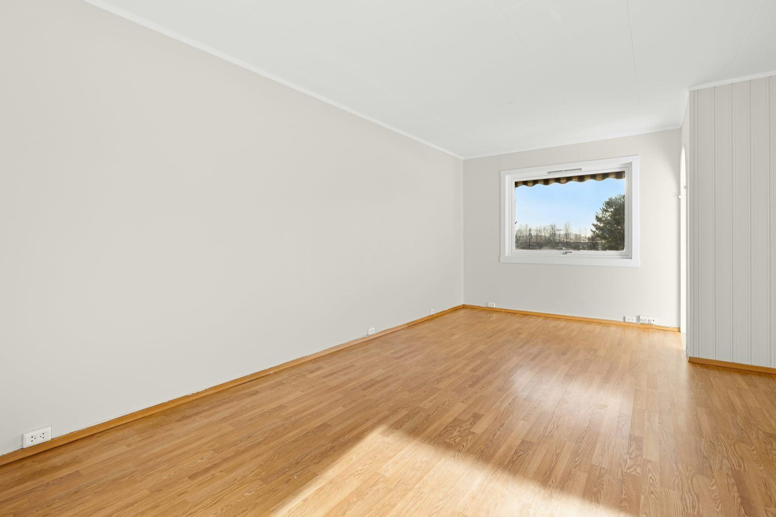 Long empty room with glossy oak-look floor, pale gray walls, and a single window