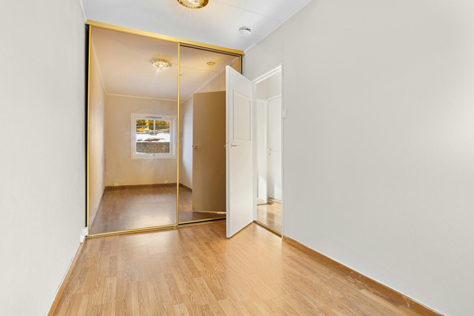 Small empty room with oak-look floor and gold-framed mirrored sliding closet doors