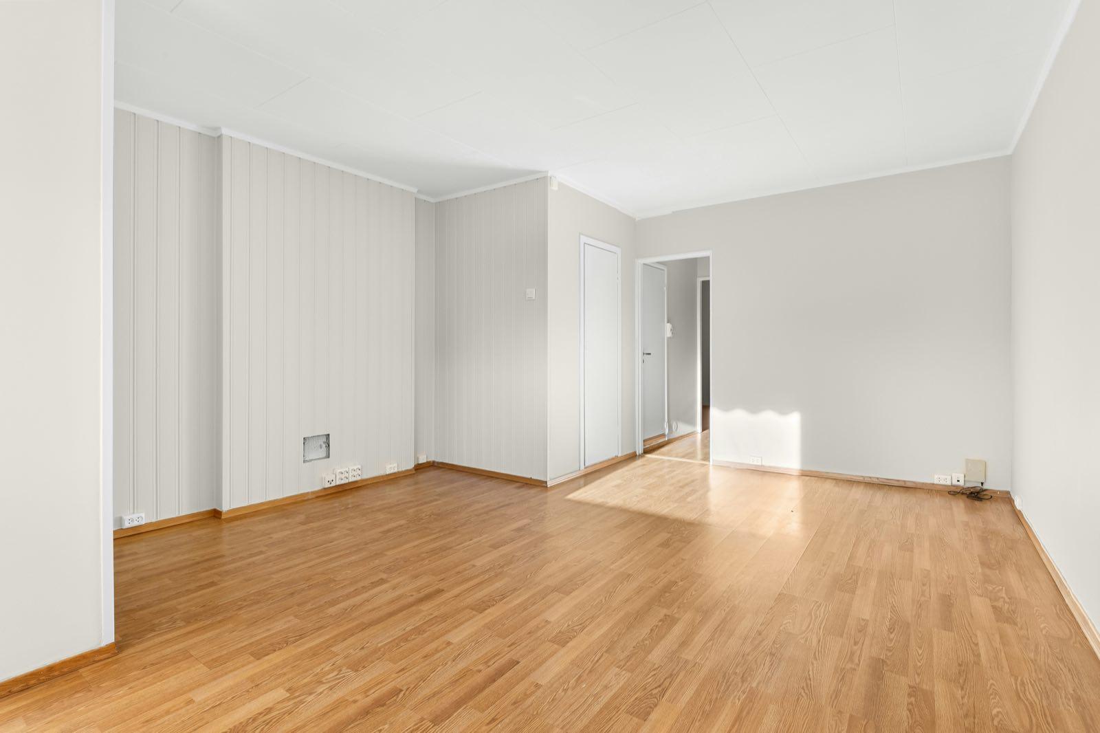 Sunlit empty room with oak-look floor, gray panelled walls, and open doorway to a hall