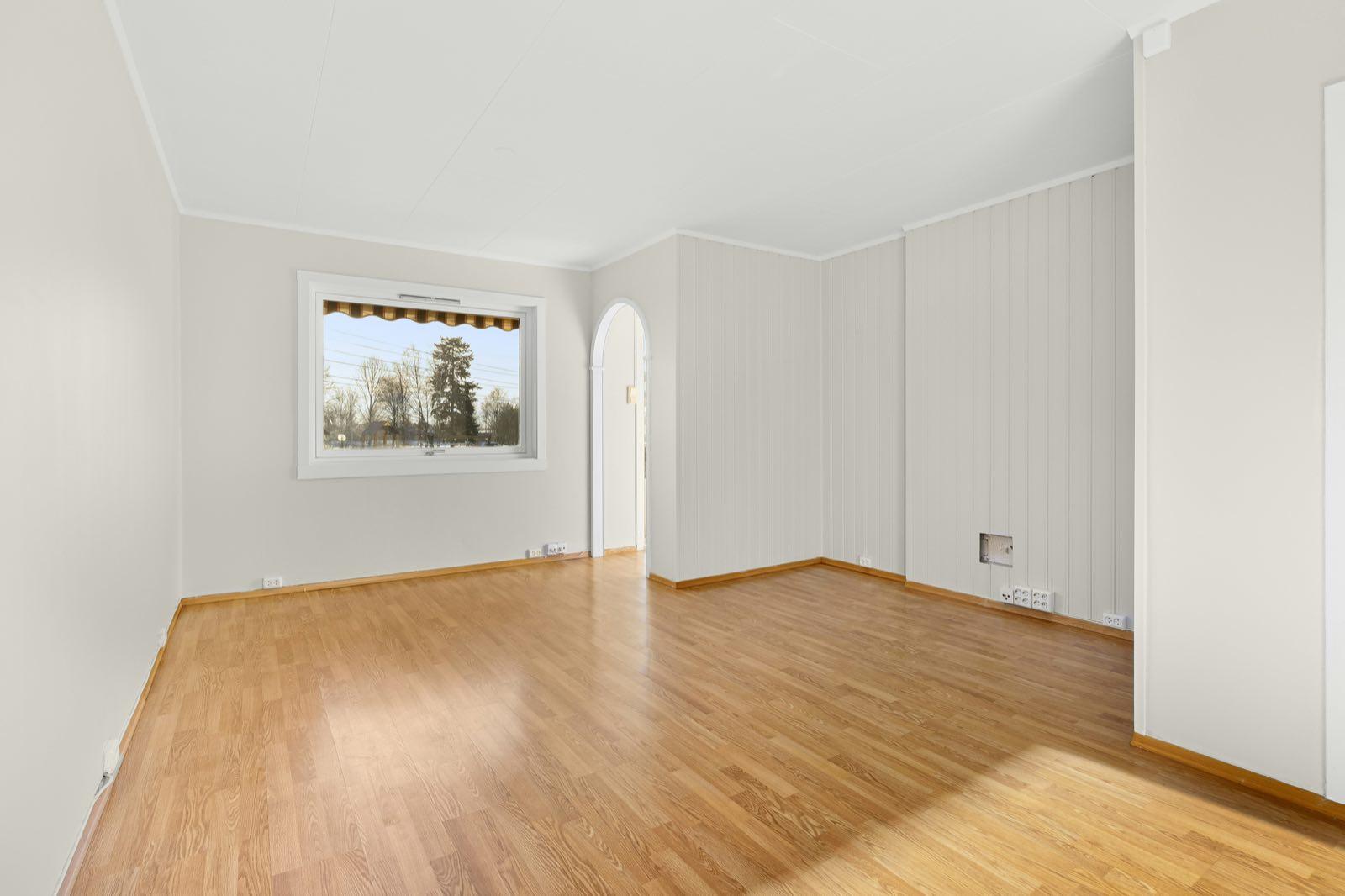 Empty room with light oak-look floor, arched doorway, panelled wall, and picture window