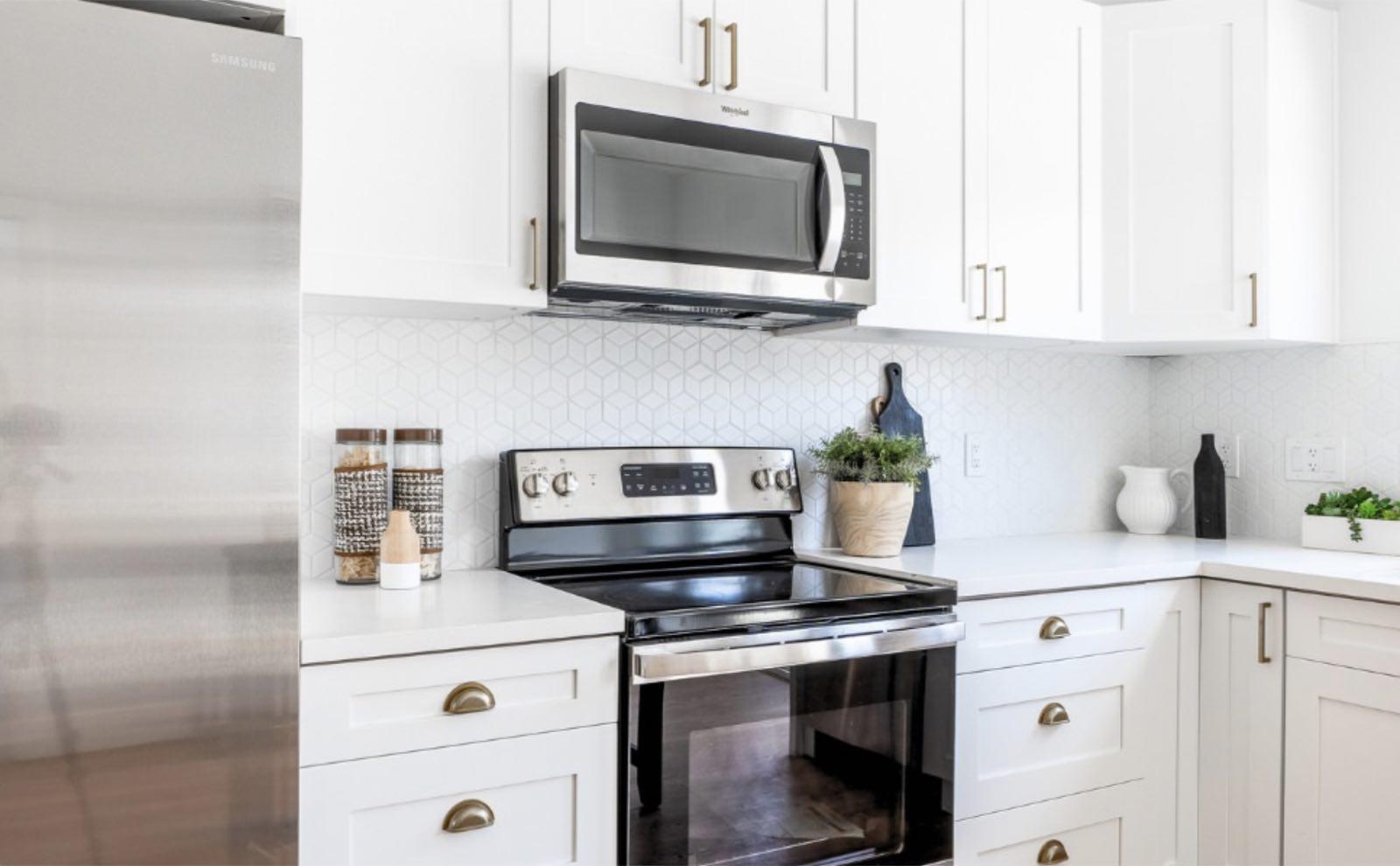 Close-up of white shaker cabinets with brass pulls, stainless range, and geometric tile backsplash