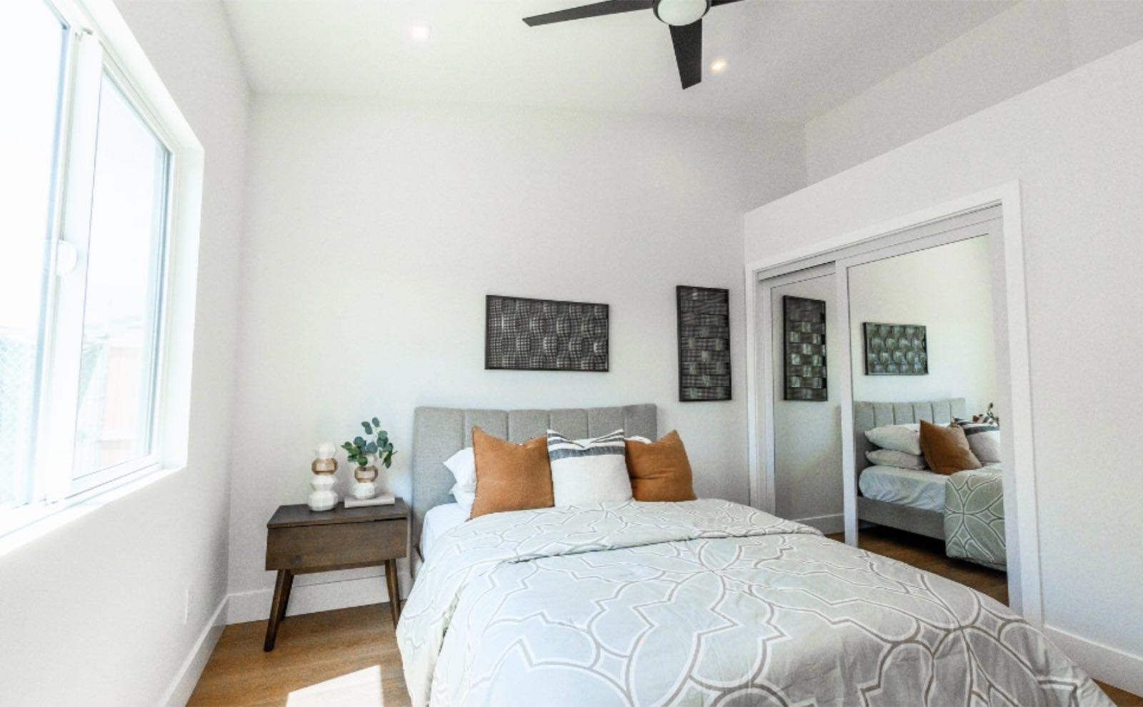 Bedroom with gray channel-tufted headboard, rust pillows, mirrored sliding closet doors, and large side window