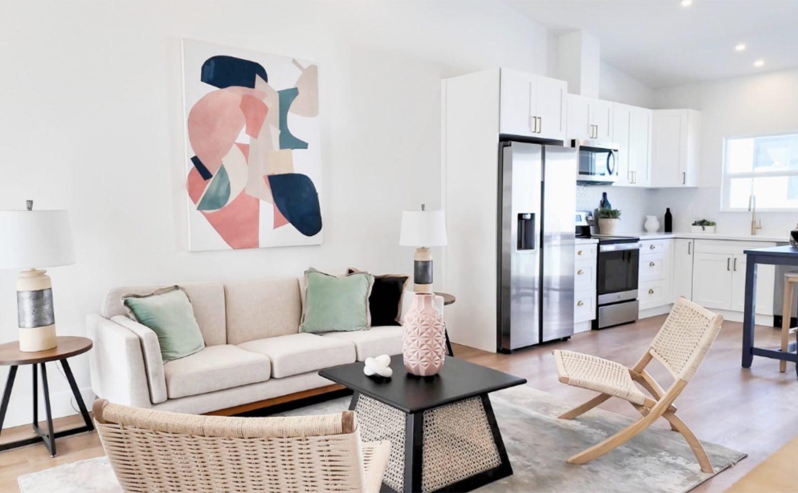 Open living area with cream sofa, abstract wall art, woven chairs, and white shaker kitchen