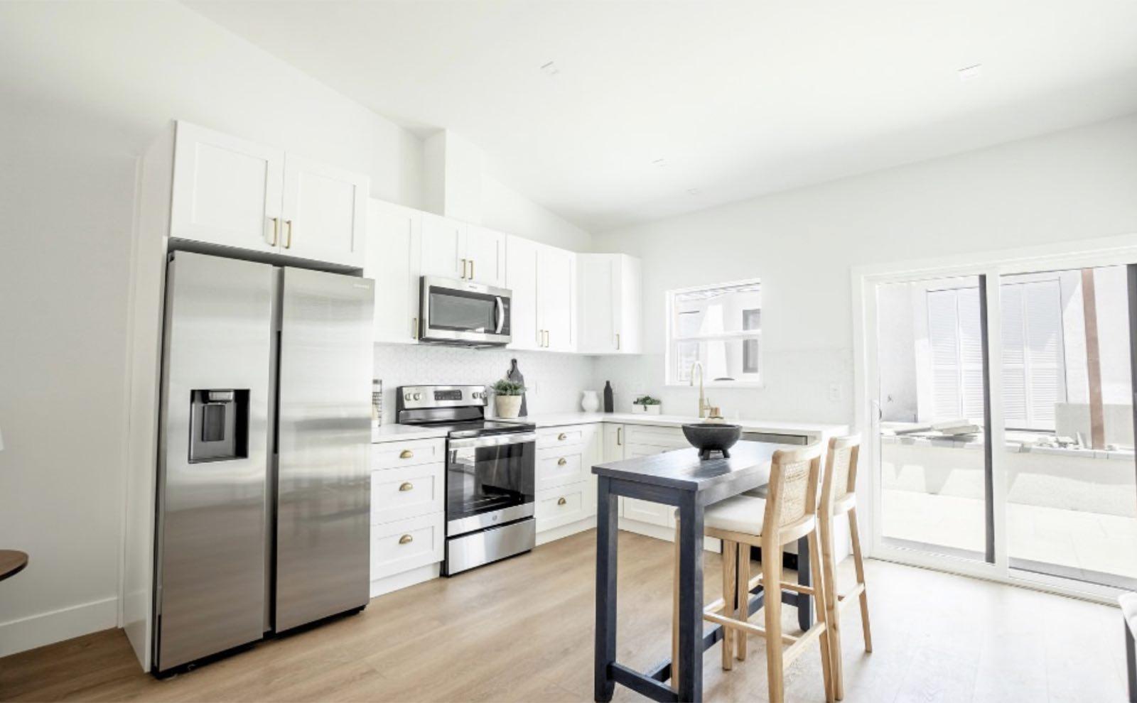 White shaker kitchen with stainless appliances, navy bar-height table, and sliding glass patio door