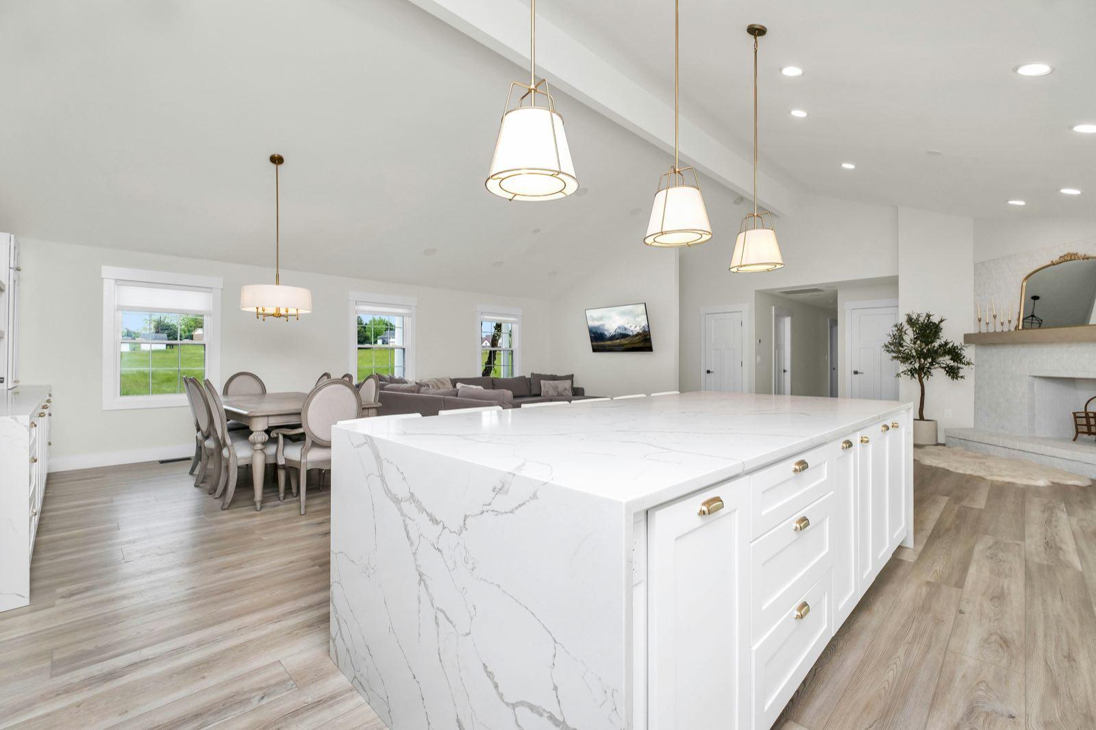 View from dining area of large white quartz island with brass pendant lights and open-plan living behind