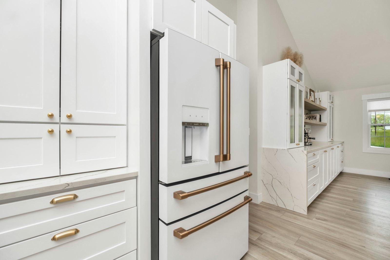 White panel-ready French door refrigerator with bronze handles flanked by tall shaker cabinetry with brass pulls