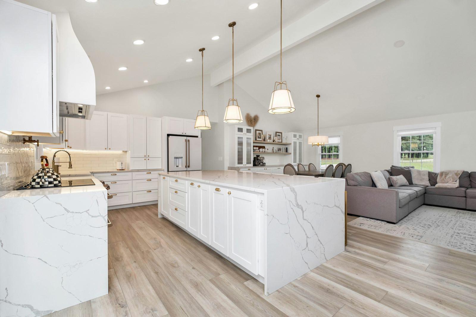 Wide angle of open-plan kitchen and living area showing full island, vaulted ceiling, and sectional sofa beyond