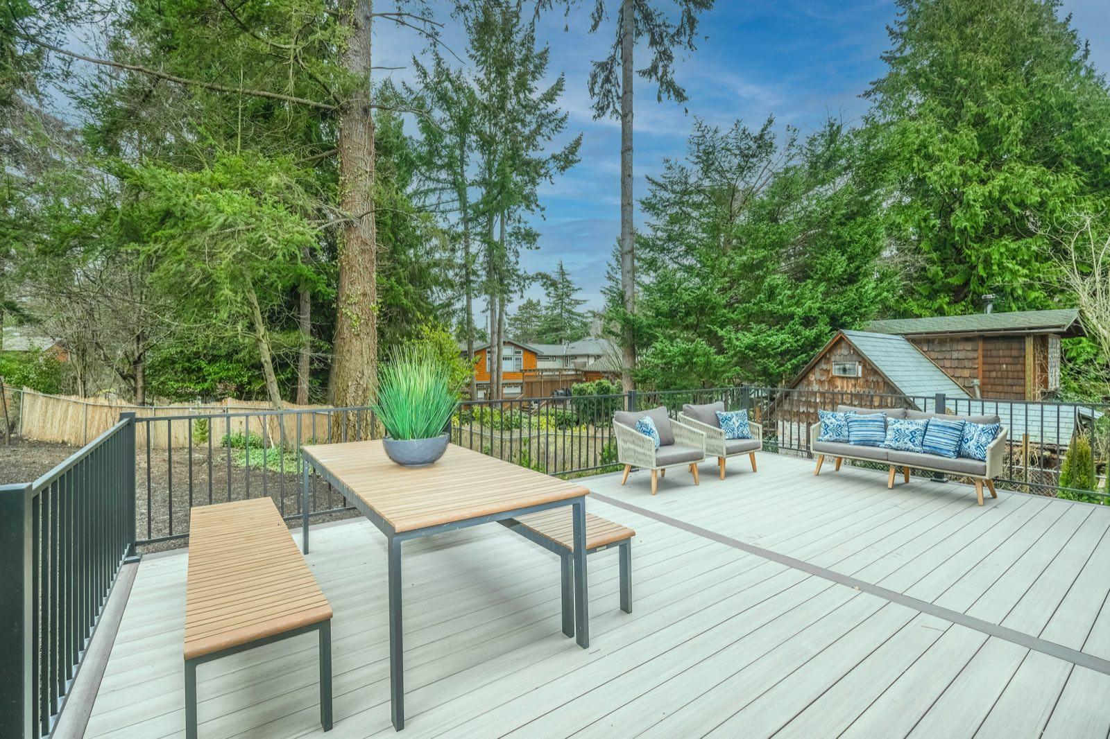 Gray composite deck with picnic table, cushioned loveseat seating, and black metal railing among evergreens