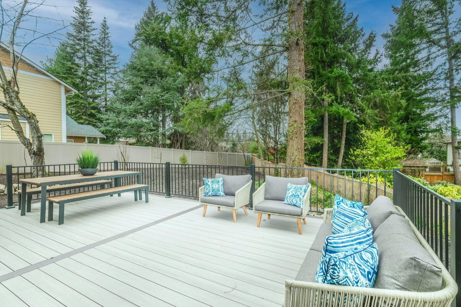Wicker lounge chairs and sofa with blue pillows on a gray composite deck with black railing