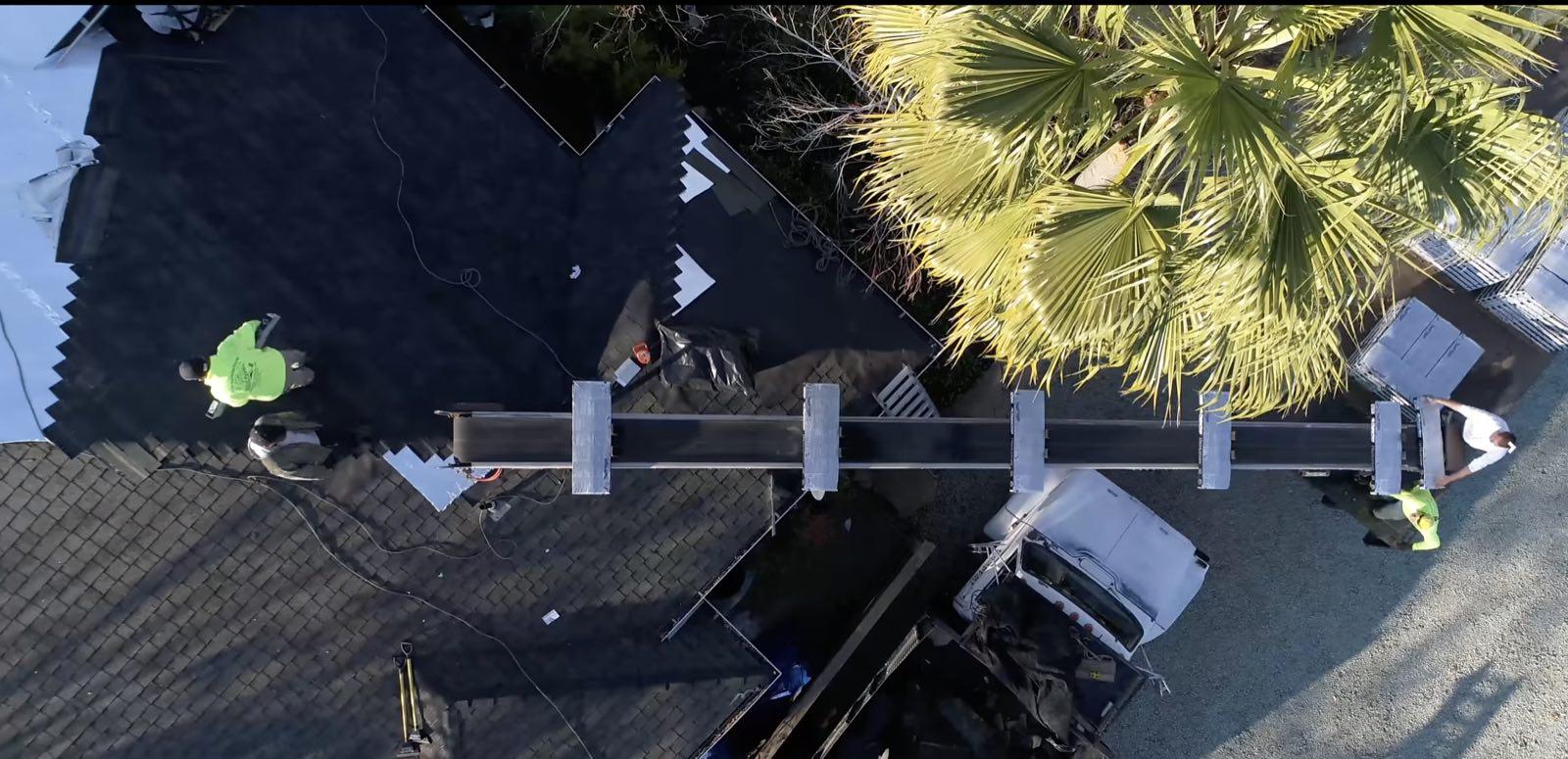Overhead view of a conveyor ladder reaching from a truck to roofers on a dark roof
