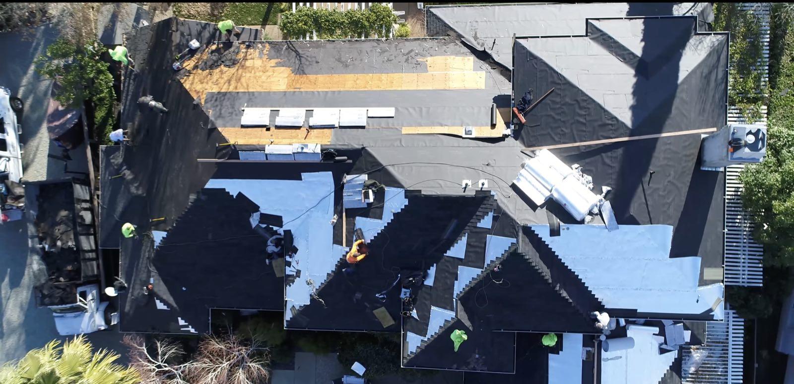 Top-down view of a roof mid-replacement showing bare plywood, underlayment, and crew at work
