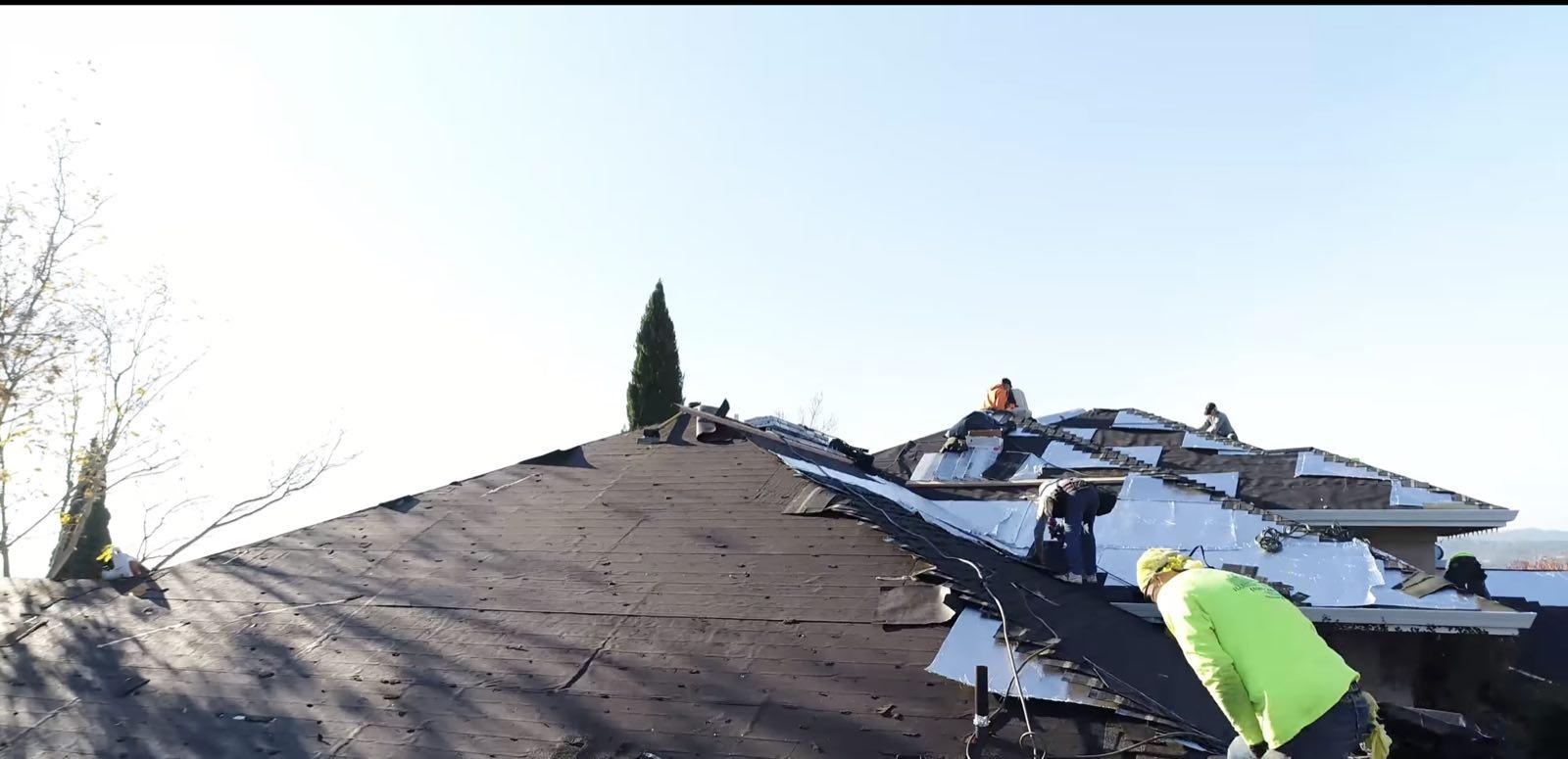 Roofing crew in high-visibility shirts working across a hip roof with dark felt and silver underlayment