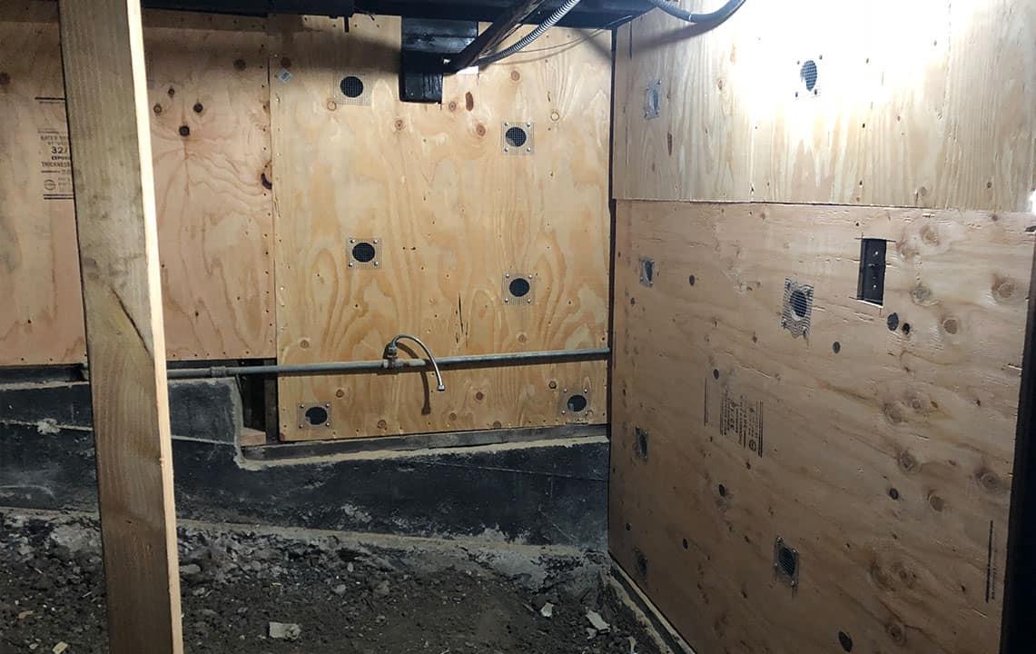 Plywood panels with round vent holes nailed to short framed walls above a concrete foundation