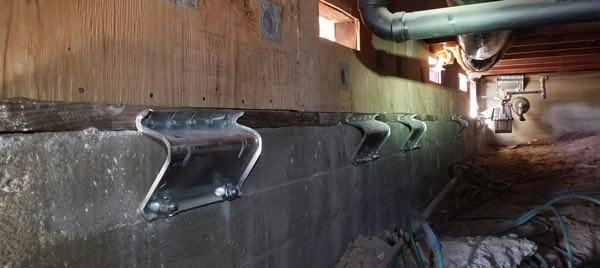 Row of galvanized steel brackets tying wood framing to a concrete foundation wall