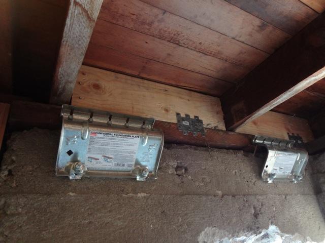 Galvanized foundation plates bolted between a wood sill and concrete wall beneath floor joists