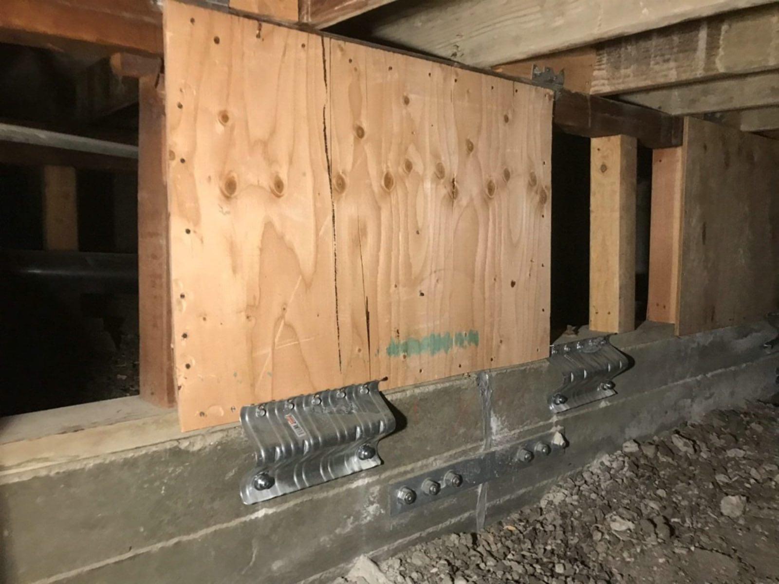 Plywood bracing panel on a short framed wall with steel plates bolted to concrete foundation