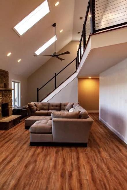 Vaulted living room with taupe sectional, skylights, ceiling fan, and stairs rising to a loft
