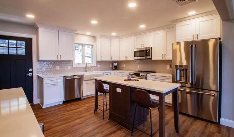 Kitchen with white shaker cabinets, stainless appliances, dark wood island with stools, and hardwood floor