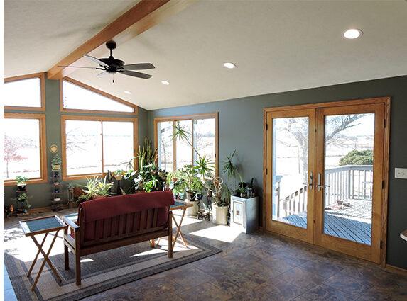Sunroom with gray-green walls, oak-trimmed windows and French doors, exposed beam, and houseplants