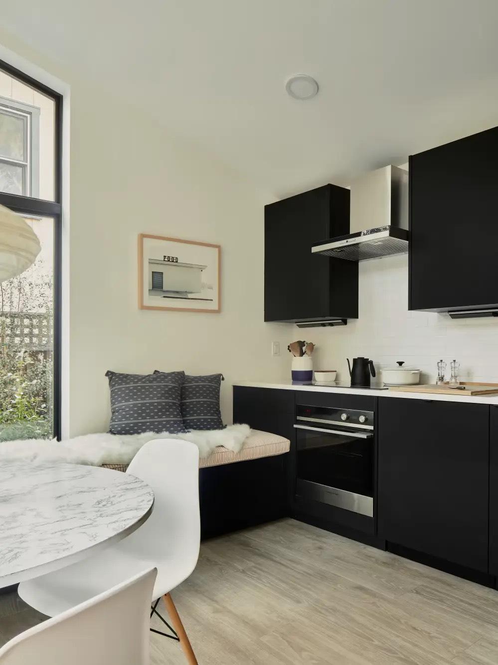 Kitchenette with matte black cabinets, stainless wall oven, cushioned window bench, and round marble table