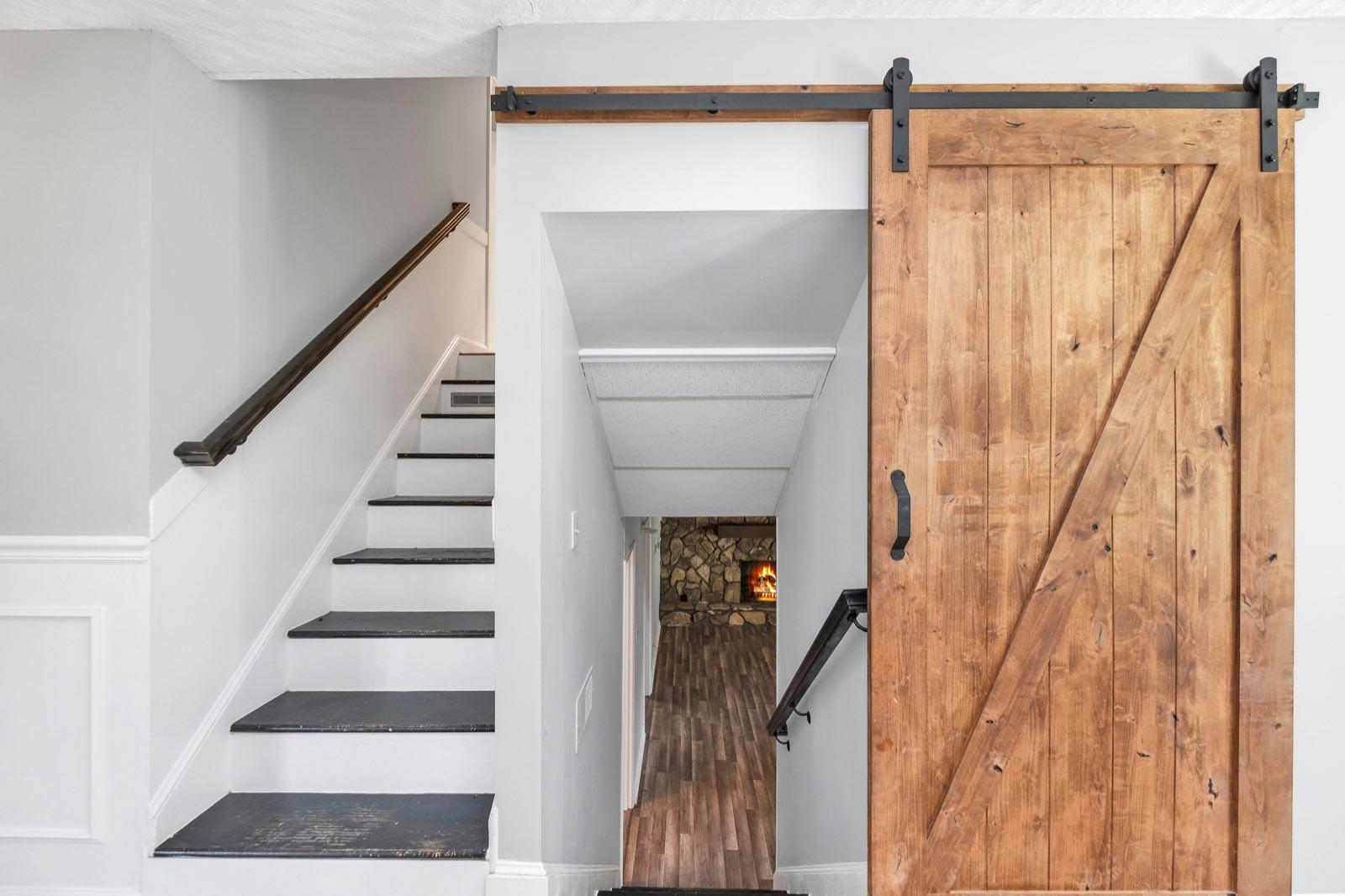 Rustic knotty-pine sliding barn door on black track beside a staircase with dark treads