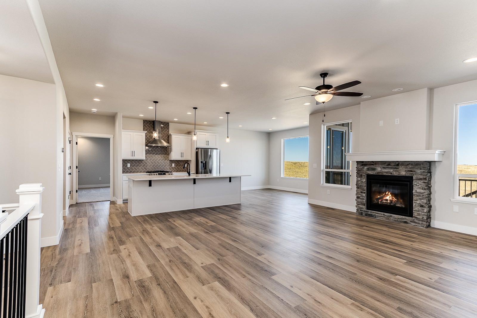 Open great room with gray-brown plank flooring, white kitchen island, and stacked-stone fireplace