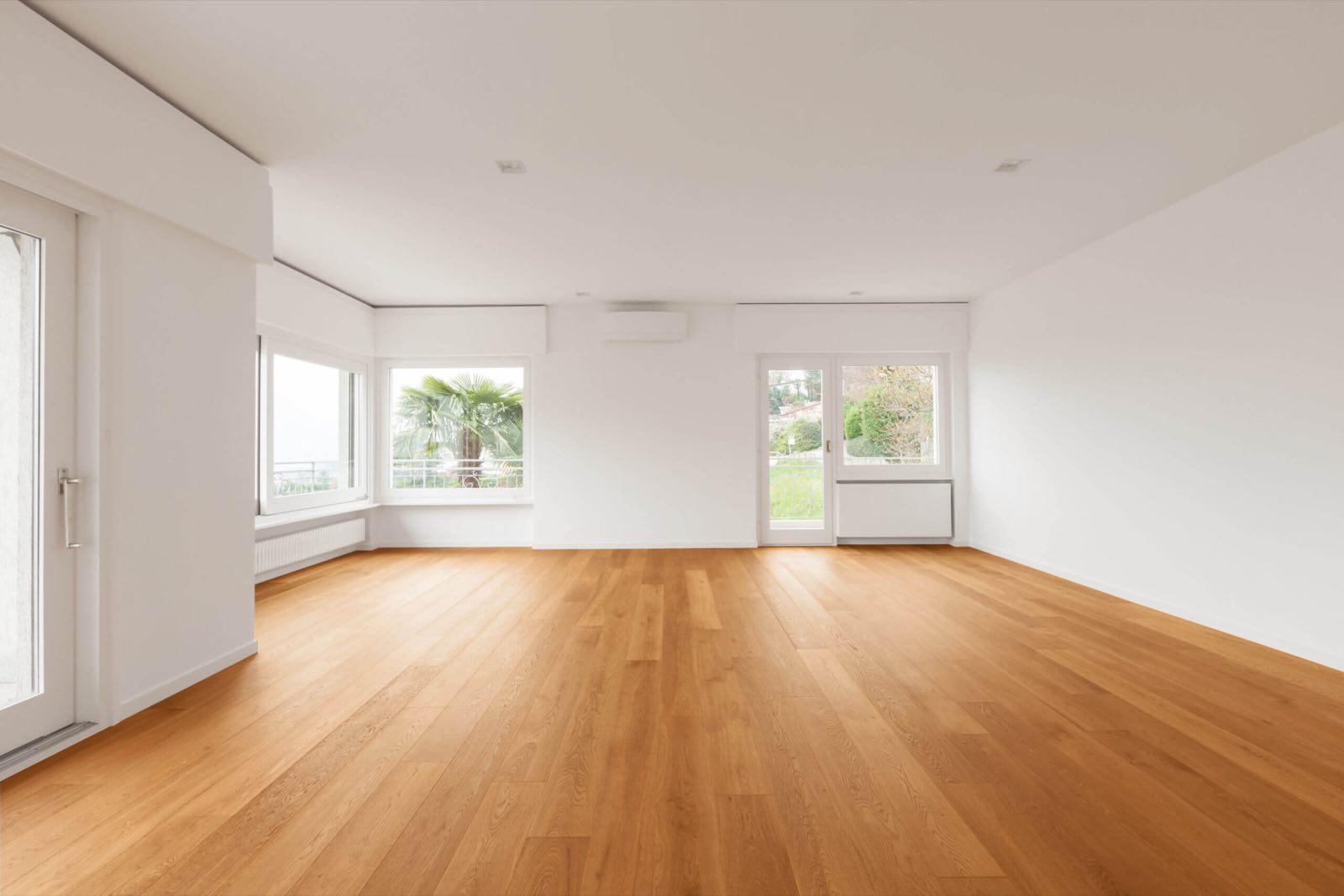 Empty white room with honey-toned wide-plank oak floor and garden-view windows