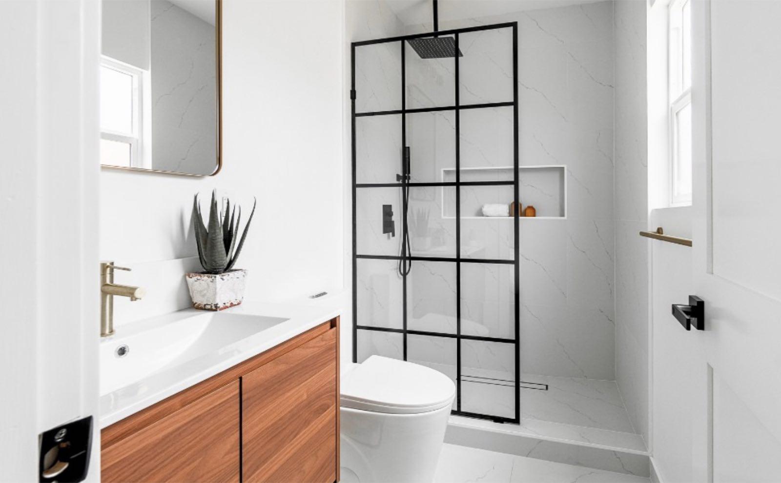 Bathroom with walnut floating vanity, brass faucet, and black grid-framed glass shower with marble-look walls