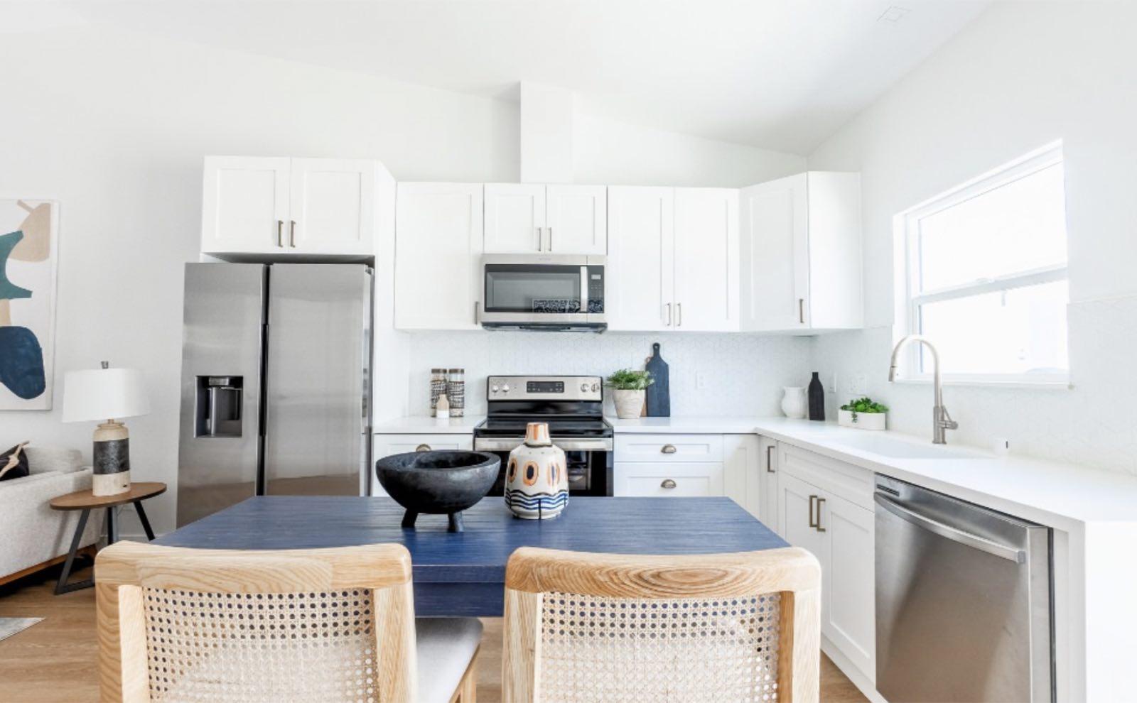 White shaker kitchen with stainless appliances and navy dining table with cane-back chairs