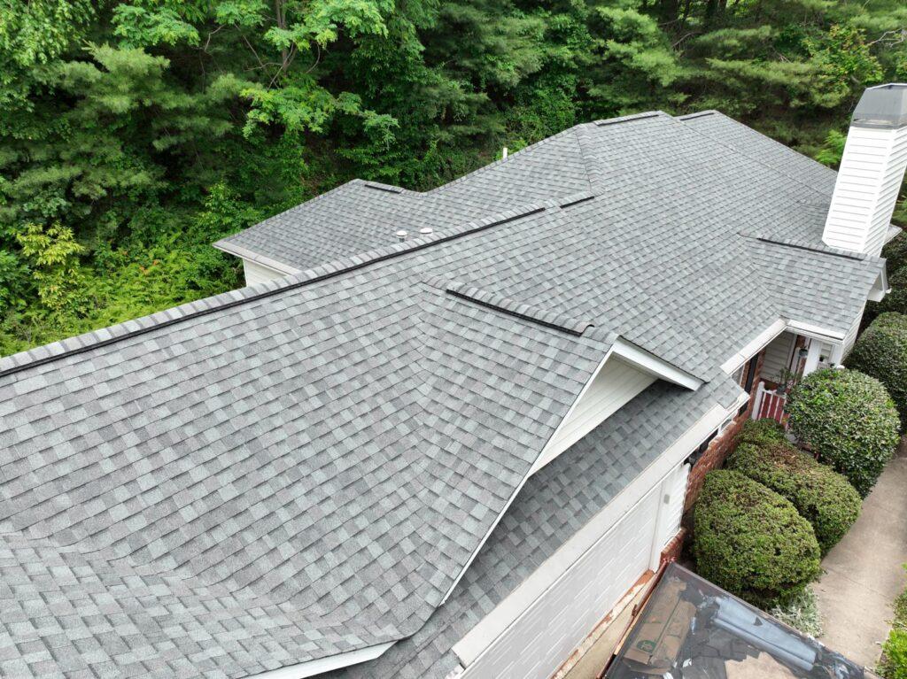 Aerial view of gray architectural shingle roof on a white-sided house surrounded by trees