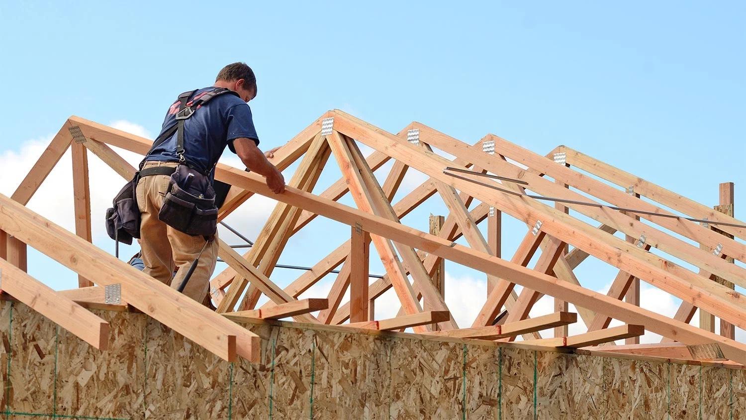 Framer in a tool belt setting wood roof trusses on a new house under a blue sky