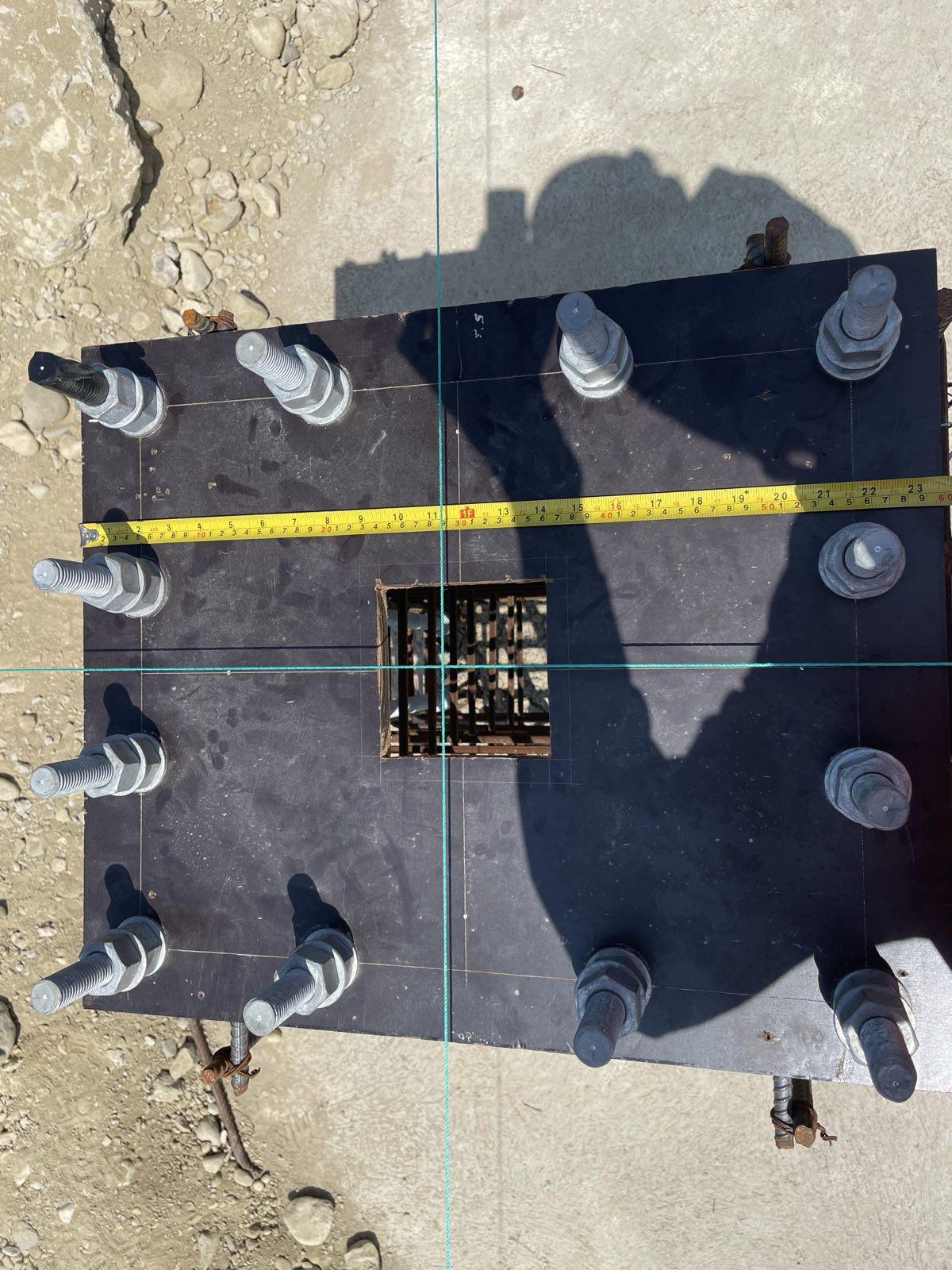 Top-down view of anchor bolt template on a concrete footing with tape measure and laser lines