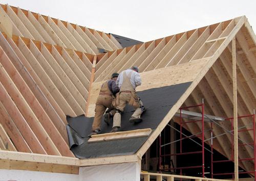 Two workers laying roofing felt in the valley of a newly framed roof with exposed rafters