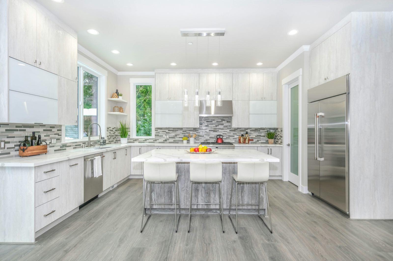 Wide view of kitchen with pale wood-grain cabinets, gray plank floor, island, and built-in stainless refrigerator