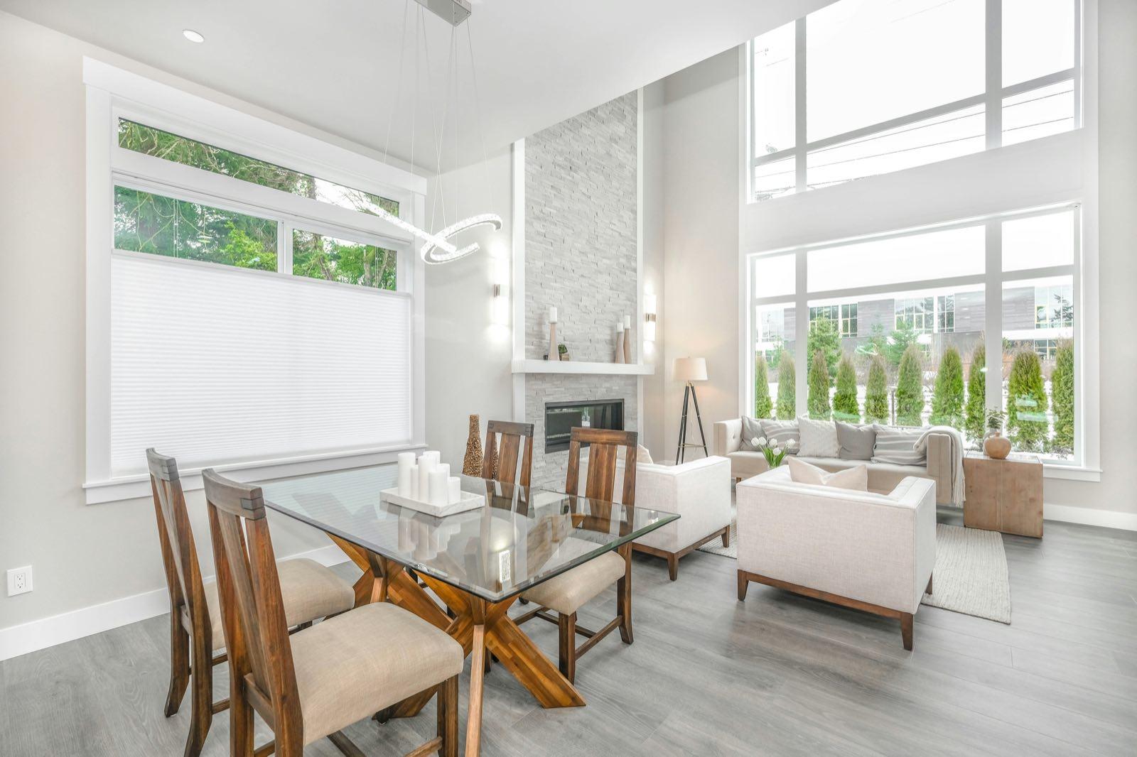 Dining area with glass-top table beside a double-height living room with stacked-stone fireplace