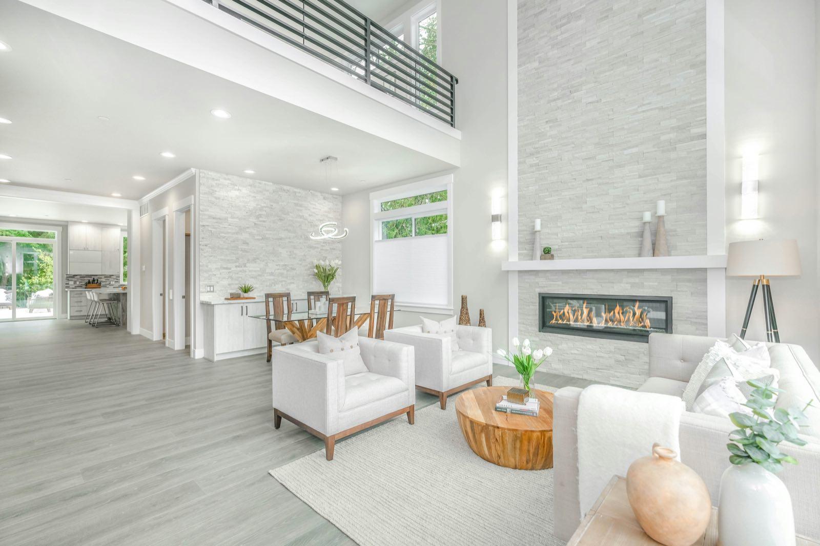 Double-height living room with white armchairs, linear gas fireplace in stacked stone, and loft railing above
