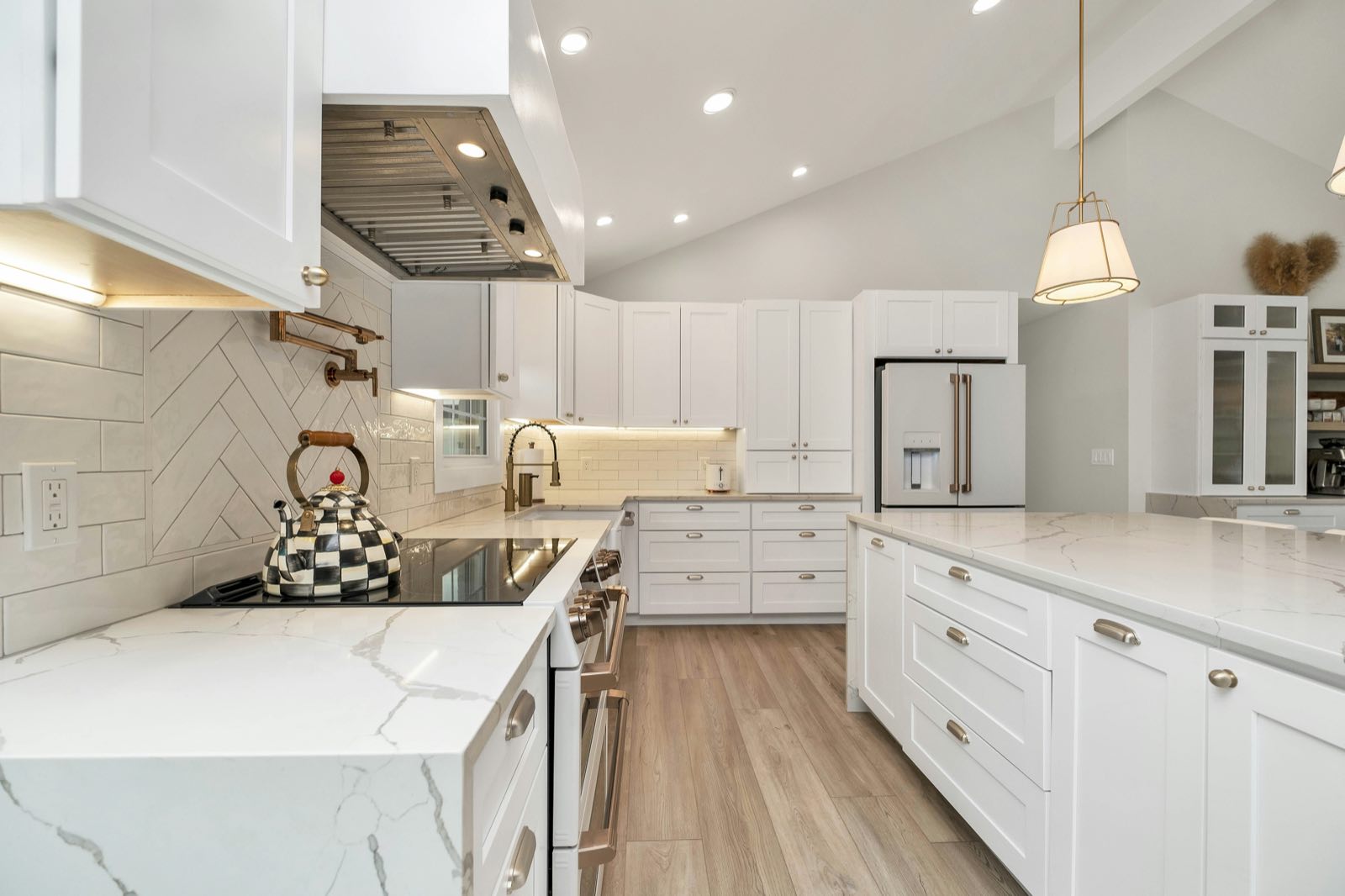 Range zone with herringbone subway tile backsplash, under-cabinet lighting, stainless hood, and white double oven
