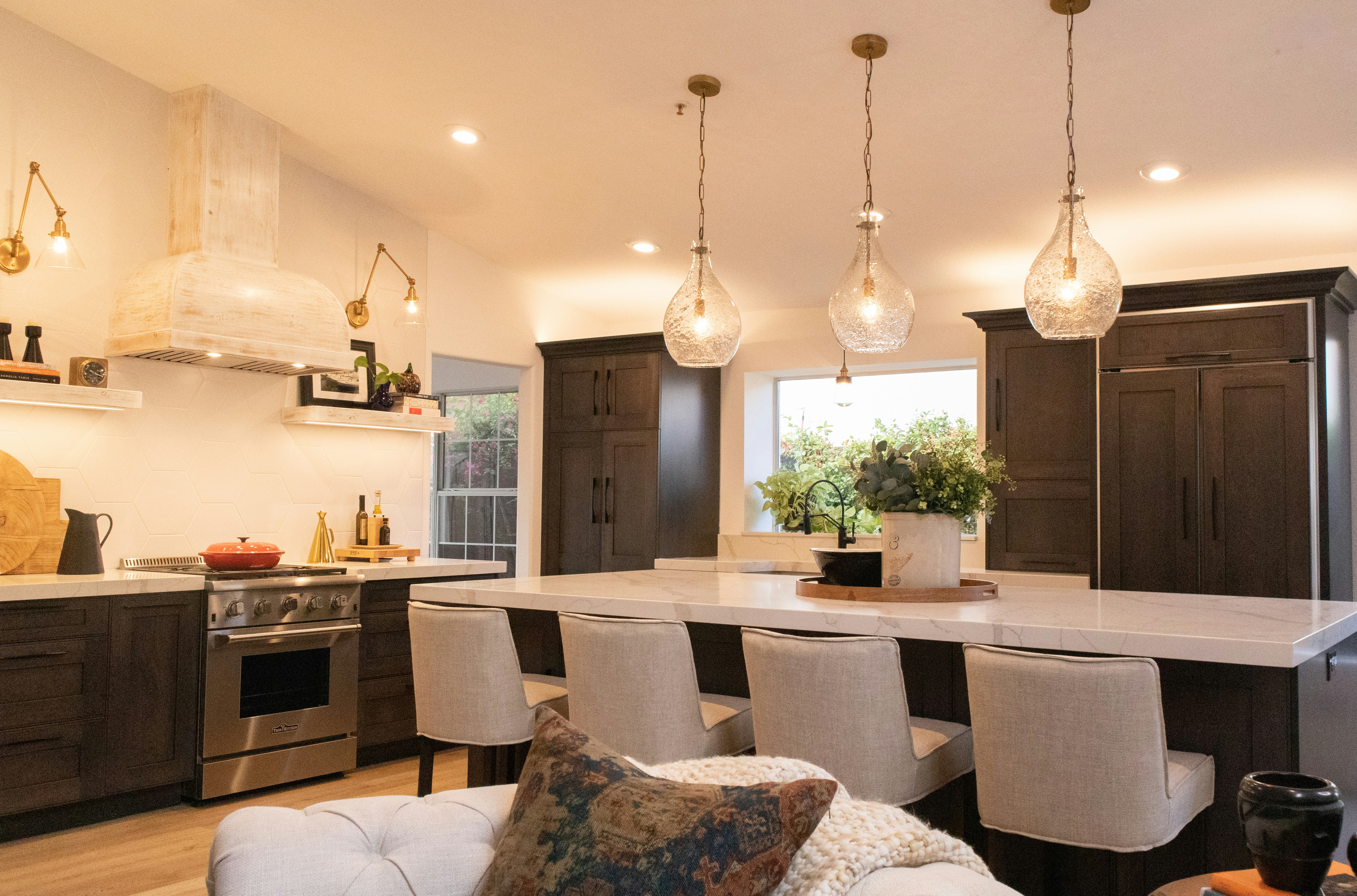 Warm open-plan kitchen with dark stained wood cabinets, white quartz island, and globe pendant lights